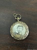 Front view of antique round photo locket showing portrait of young boy and floral embossed metal frame