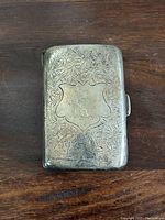 Top view of the rectangular sterling silver case with detailed floral leaf engravings and central shield cartouche with initials.