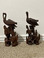 Front angle of two wooden bird sculptures showing detailed wing and feather carving with geometric style bases.