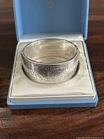 Front view of engraved sterling silver bangle in Birks box