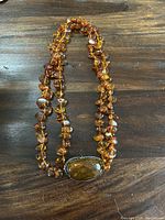 Full view of necklace laid out on wooden surface, showing amber beads and large centerpiece
