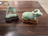 Two jade carvings on table: a water buffalo and a crane, both mounted on wooden bases.