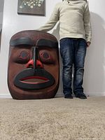 Mask leaning against wall next to person wearing sweater and jeans for scale