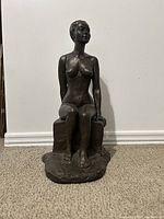 Front view of bronze sculpture showing seated nude figure