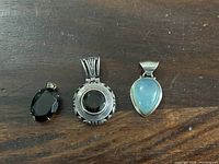 Front view of three sterling silver pendants on wooden surface, showing black and light blue stones and different bales.
