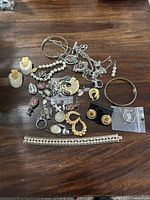 Photo showing assorted jewelry pieces spread on wooden surface including earrings, bracelets, necklaces, and pendants