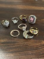 Overview of all eight rings showing the different designs and metals on a wooden surface