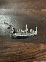 Close up front view of the Siam sterling silver brooch showing boat shape with pointed temple-like structures and black enamel decoration on wood surface.