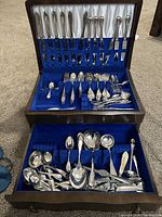 Open wooden case showing lid rack of knives and two pull-out drawers with flatware