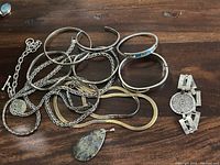 Multiple silver cuff and hinged bangle bracelets with assorted chain styles and pendants displayed on wood surface