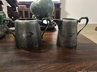 Front view of silver sugar bowl and creamer on wooden table, showing detailed engraving and handles/spout.