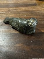 Side view of carved soapstone bird-shaped seal showing detailed engraving of eyes and beak and natural stone veins.