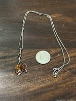 Sterling silver chain with amber pendant shown next to a quarter for size reference.