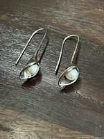 Sterling silver earrings featuring pearls inside a curved silver frame on wooden surface.