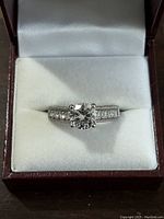 Front view of sterling silver ring with large clear stone and smaller stones on the band inside a jewelry box.