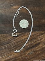 Full view of the sterling silver necklace with pendant next to a quarter for size reference on a wooden surface.