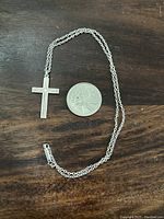 Necklace laid flat next to a coin for size comparison on a dark wooden surface.