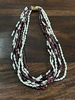 Full view of multi-strand necklace showing alternating strands of white freshwater pearls and deep red translucent gemstone beads