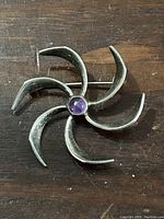 Front view of sterling silver brooch with central round purple stone, showing flower or pinwheel design with six curved blades.