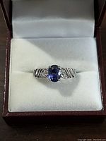 Front view of sterling silver ring with oval blue gemstone and small clear accent stones on band, set in a ring box.