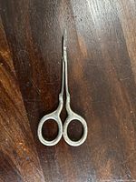 Full view of the sterling silver scissors showing the entire length on a dark wooden surface.