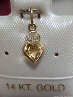 Close-up image showing the front face of the 14K gold pendant with heart-shaped faceted citrine gemstone and decorative swirl detail on bail, mounted on display card verifying 14K gold.