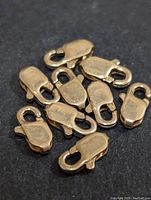 Photo showing 10 small 14K gold filled lobster clasps on a dark background, close-up view.