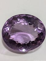Close-up photo of oval faceted purple amethyst gemstone showing light reflections and internal facets in detail.