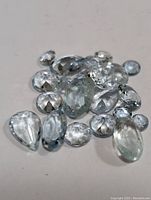 Various loose genuine aquamarine gemstones in different cuts and sizes, scattered on a white surface.