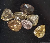 Seven assorted fancy color diamonds in pear and oval shapes displayed on a black background.