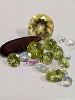 Top view of assorted faceted gemstones in yellow-green, brown, light blue, pink, and clear shades, showing varying shapes and cuts.
