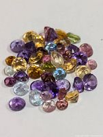 Close-up showing mixed genuine gemstones in various colors including purple, yellow, blue, green, pink, orange, and clear polished and faceted.