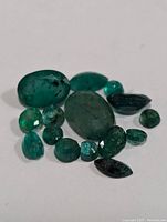 Close-up front angle of multiple emerald gemstones showing various shapes and natural inclusions.