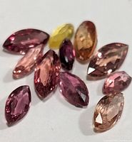 Photo of various marquise-cut fancy color sapphire gemstones in different shades placed on a white background.