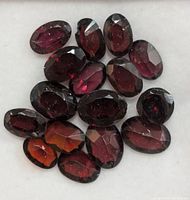 Top view of multiple oval faceted garnet gemstones showing deep red coloration and faceting details.