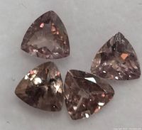 Close-up photo of four triangular faceted garnet gemstones showing their brownish-pink to purple changing colors.