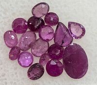 Close-up image of multiple loose faceted genuine ruby gemstones with varied sizes and cuts on white background.