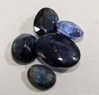 Five genuine sapphire gemstones in various blue shades, arranged on a flat surface.