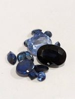 Close up of multiple genuine sapphire gemstones in various shapes and shades of blue on a white background.