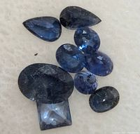 Eight loose blue sapphire gemstones varying in pear, oval, round, and square cuts on white surface