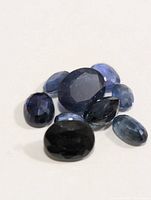 Group of nine faceted loose sapphire gemstones of varying blue hues and cuts on white background.