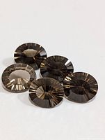 Five round-cut genuine smokey quartz gemstones arranged on a white surface, showing facets and color.