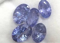 Close-up of five oval cut light bluish-purple tanzanite gemstones showing facets and internal inclusions.
