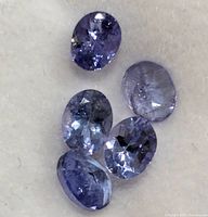 Top view of five loose oval faceted tanzanite gemstones on a white background showing their violet-blue color and clarity.