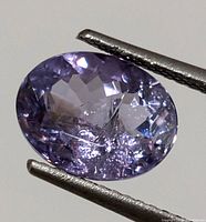 Close-up image of oval-shaped tanzanite gemstone showing clarity, color, and cut facets held by metal tweezers.