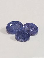 Three faceted tanzanite gemstones on a white background, showing natural inclusions and color variation.
