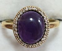 Front view of silver ring with oval cabochon purple amethyst surrounded by clear CZ stones.