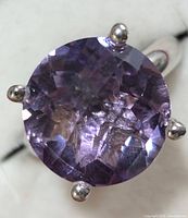 Top close-up view of round faceted purple amethyst stone set with four silver prongs.