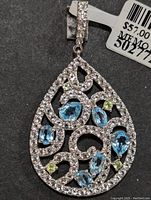 Front view of silver teardrop pendant with blue topaz and cubic zirconia stones, showing the filigree design and the attached bail with CZ stones.