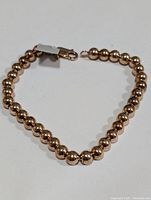 Silver beaded bracelet laid out showing round polished beads, clasp closure, with tag attached.